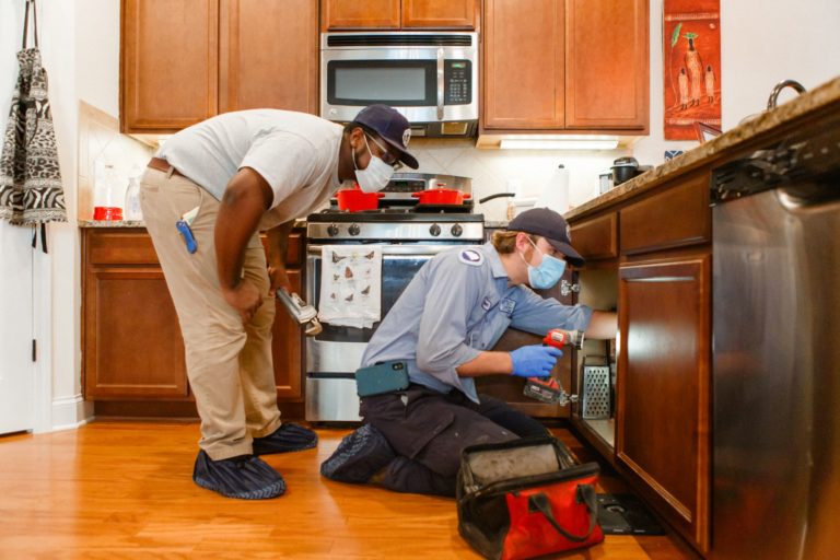 Meetze Plumbing technician reaching under kitchen sink with flashlight