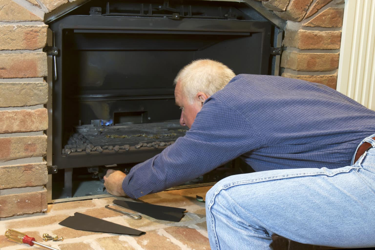 Man doing installation, repair, or seasonal maintenance on a built-in gas fireplace