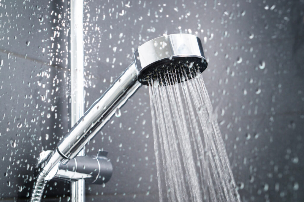 Shower behind wet glass window with water drops splashing. Water running from shower head and faucet in modern bathroom.